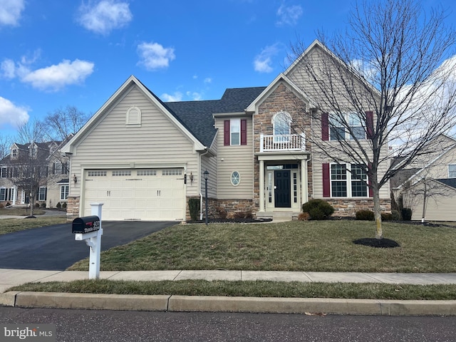 view of front of house featuring a balcony, driveway, roof with shingles, a front lawn, and stone siding