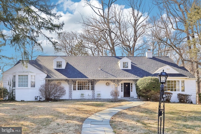 new england style home featuring covered porch, a front lawn, and a shingled roof