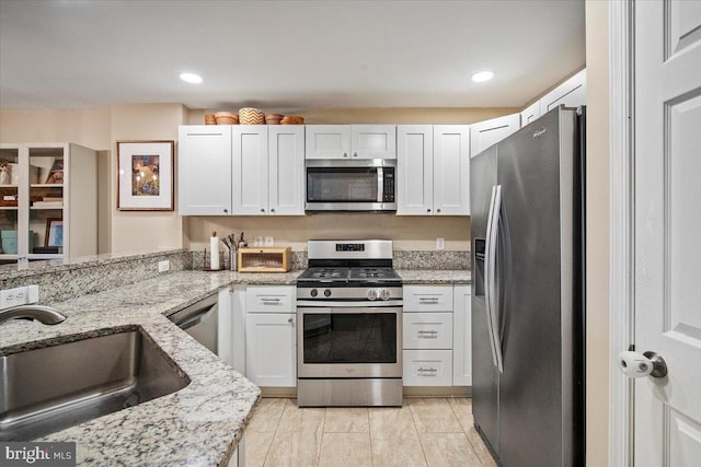 kitchen with white cabinets, light stone counters, appliances with stainless steel finishes, and a sink