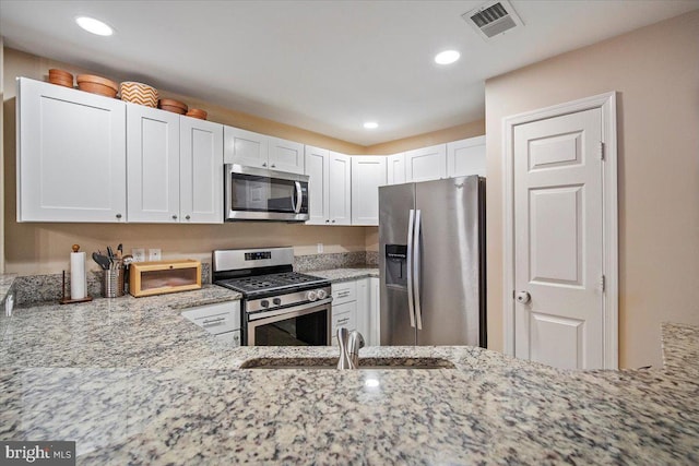 kitchen with visible vents, light stone counters, appliances with stainless steel finishes, white cabinets, and a sink