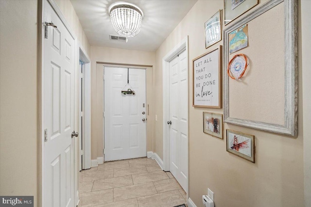 doorway to outside featuring a notable chandelier, baseboards, visible vents, and light tile patterned floors