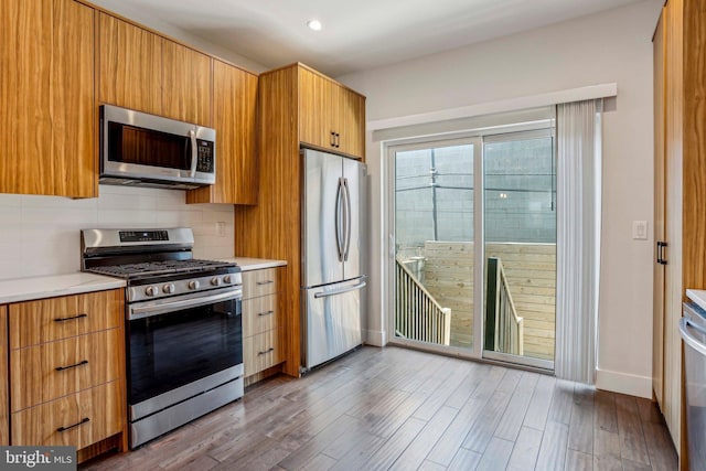 kitchen with baseboards, light countertops, decorative backsplash, appliances with stainless steel finishes, and wood finished floors