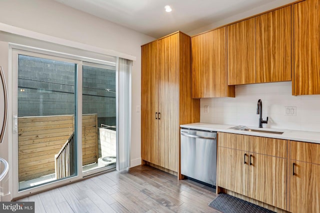 kitchen featuring light wood-type flooring, a sink, backsplash, stainless steel dishwasher, and light countertops