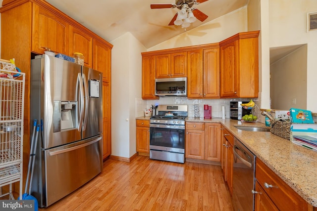 kitchen with light wood finished floors, light stone counters, decorative backsplash, stainless steel appliances, and a sink