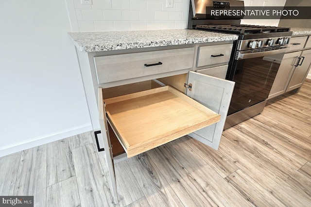 kitchen with decorative backsplash, light stone counters, light wood-style floors, and stainless steel gas range