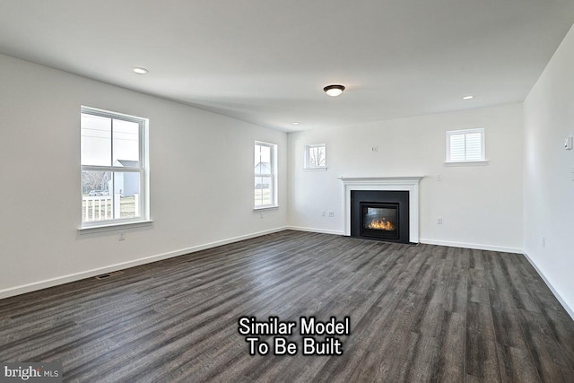 unfurnished living room featuring a glass covered fireplace, dark wood-type flooring, a healthy amount of sunlight, and baseboards