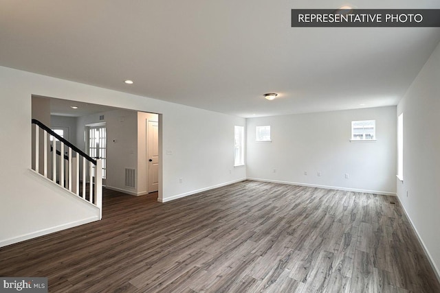 empty room featuring baseboards, wood finished floors, and stairs