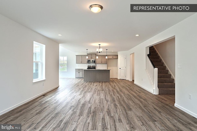 unfurnished living room with recessed lighting, baseboards, wood finished floors, and stairs