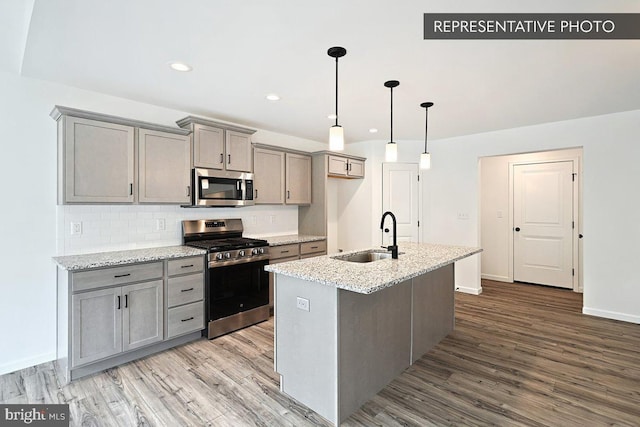 kitchen with gray cabinets, a sink, wood finished floors, stainless steel appliances, and decorative backsplash