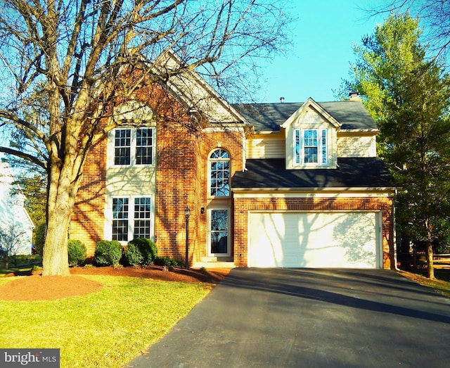 view of front of house with a front yard, an attached garage, a chimney, aphalt driveway, and brick siding