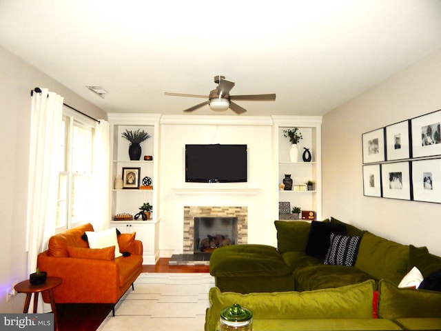 living area featuring built in shelves, a ceiling fan, wood finished floors, visible vents, and a fireplace