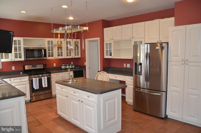 kitchen featuring dark countertops, light tile patterned floors, stainless steel appliances, and a kitchen island with sink