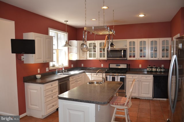 kitchen featuring a center island with sink, a sink, dark countertops, appliances with stainless steel finishes, and light tile patterned floors