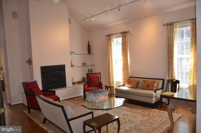 living area featuring visible vents, wood finished floors, a glass covered fireplace, rail lighting, and vaulted ceiling