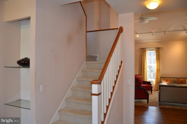 stairs featuring rail lighting, baseboards, ceiling fan, and wood finished floors