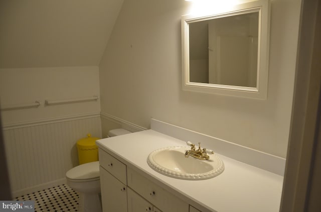 bathroom with vanity, toilet, lofted ceiling, and wainscoting