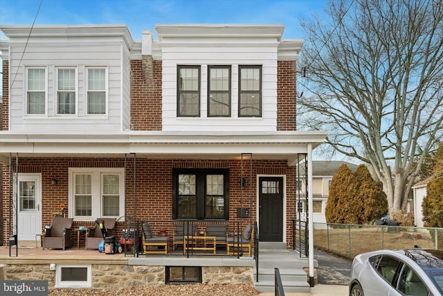 view of property with brick siding, a porch, and fence