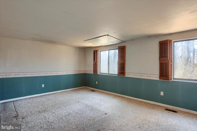 spare room featuring a wealth of natural light, visible vents, baseboards, and carpet flooring