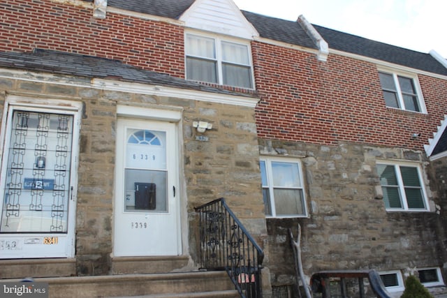 doorway to property featuring stone siding, brick siding, and roof with shingles