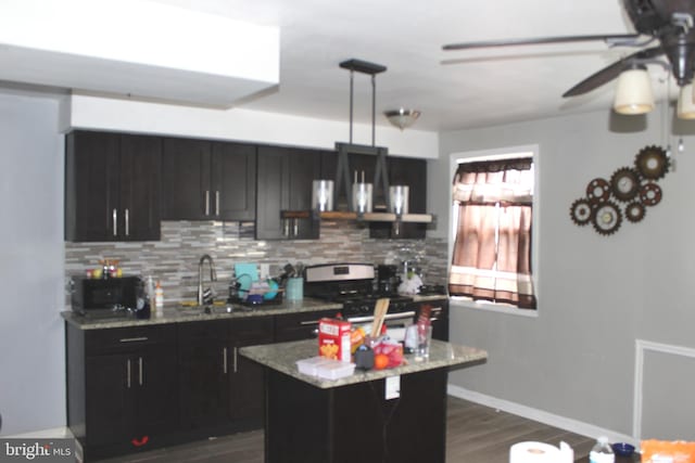 kitchen with decorative backsplash, dark cabinetry, dark wood-style floors, stainless steel gas range, and a sink