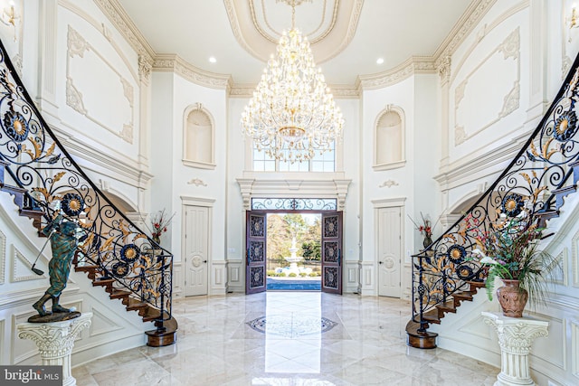 foyer entrance featuring an inviting chandelier, stairway, a decorative wall, and marble finish floor