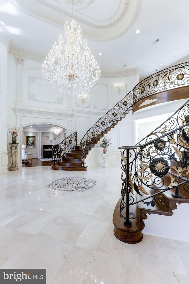 stairway featuring visible vents, a chandelier, a towering ceiling, arched walkways, and a decorative wall