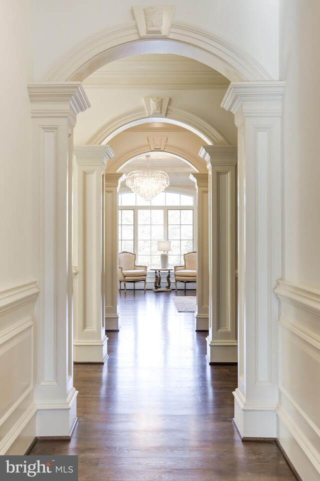 hallway with dark wood-type flooring, a decorative wall, decorative columns, and arched walkways