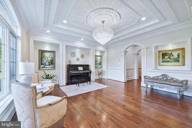 sitting room featuring a tray ceiling, a decorative wall, wood finished floors, and ornate columns