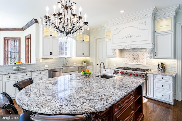 kitchen featuring a notable chandelier, a center island with sink, a sink, stainless steel appliances, and crown molding