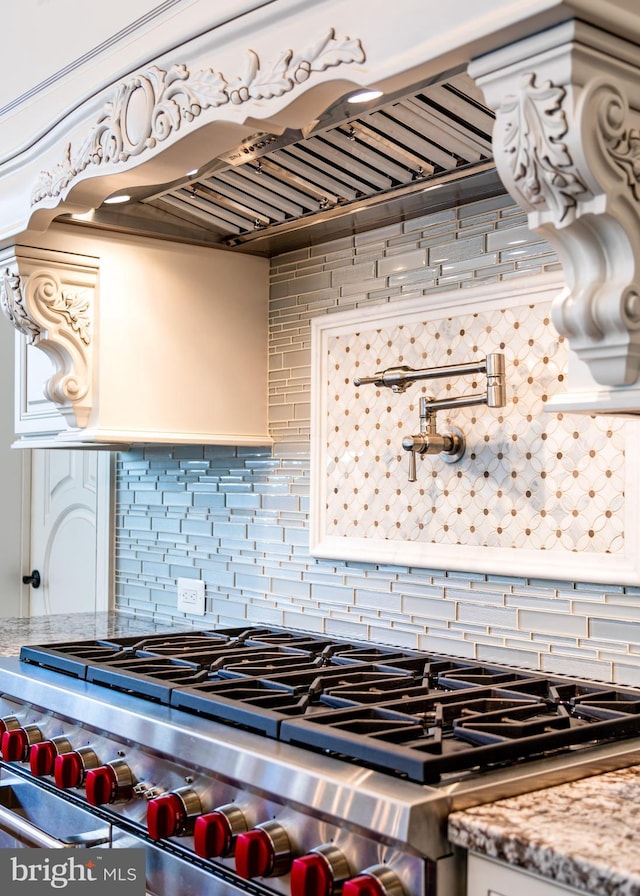 kitchen with stainless steel stove, light stone countertops, tasteful backsplash, and range hood