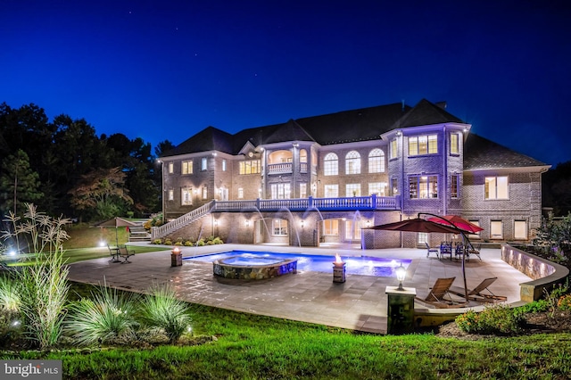 back of house at twilight featuring a balcony, stairway, a patio area, and a pool with connected hot tub