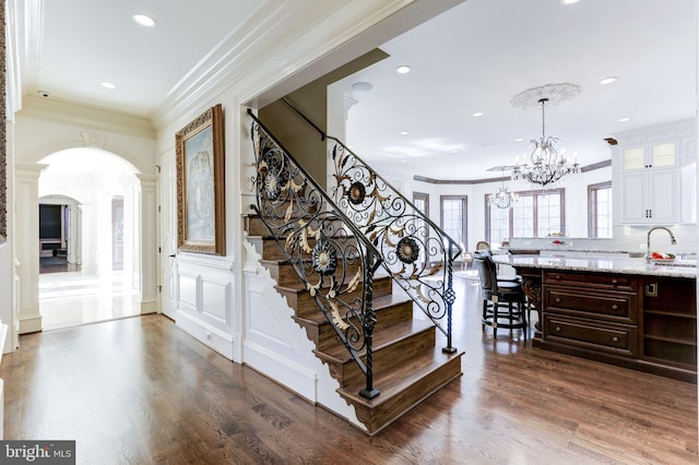 stairway featuring arched walkways, a chandelier, ornamental molding, and wood finished floors