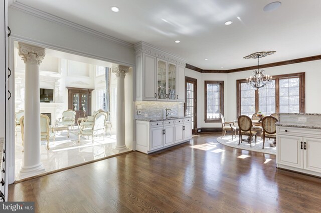 kitchen featuring dark wood finished floors, decorative backsplash, glass insert cabinets, and decorative columns