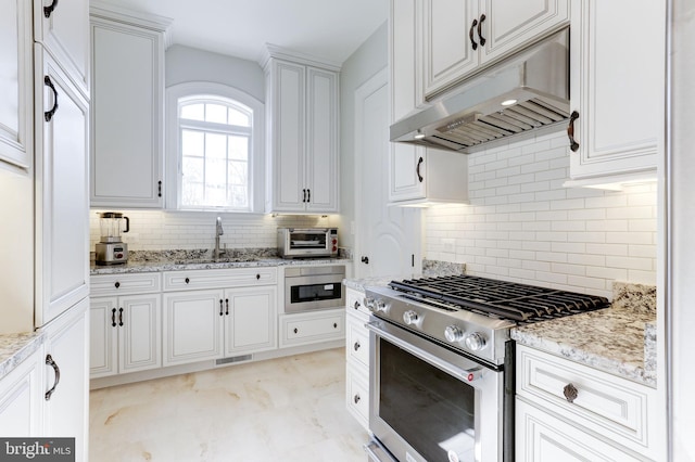 kitchen with visible vents, under cabinet range hood, high end range, white cabinets, and a sink