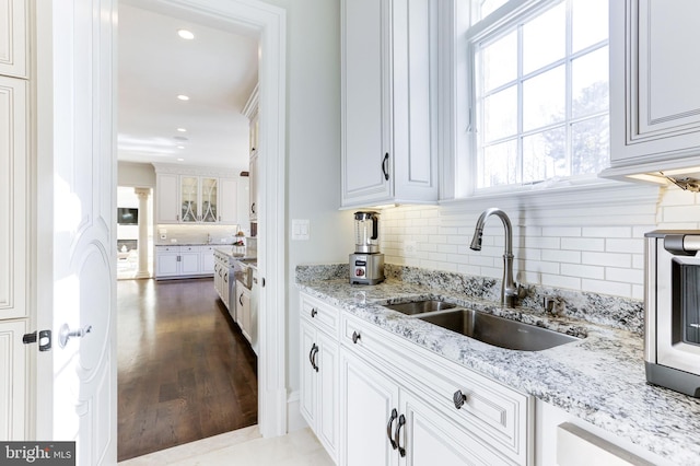 kitchen with light stone counters, wood finished floors, a sink, decorative backsplash, and white cabinetry