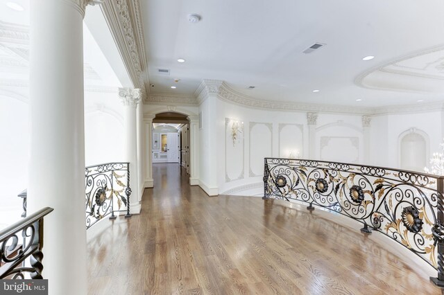 hall featuring visible vents, wood finished floors, arched walkways, crown molding, and decorative columns