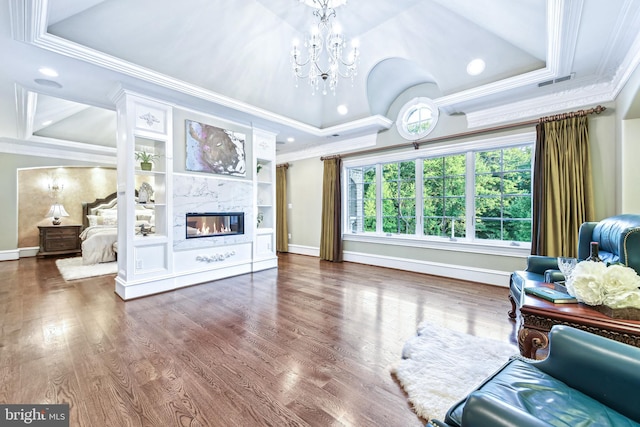 living room with wood finished floors, baseboards, a premium fireplace, a tray ceiling, and crown molding