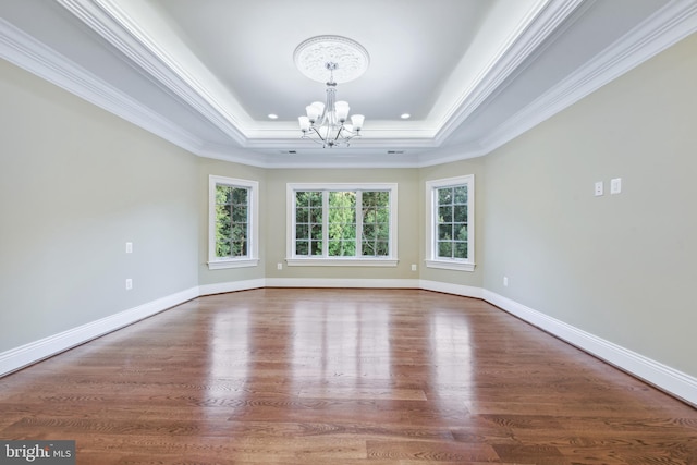 spare room with a tray ceiling, crown molding, baseboards, and a chandelier