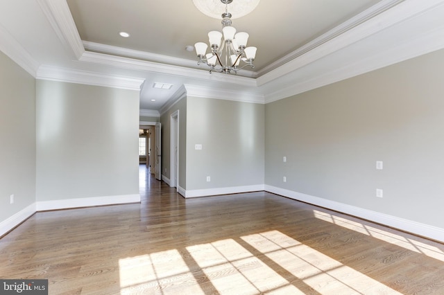 unfurnished room with an inviting chandelier, wood finished floors, baseboards, and a raised ceiling