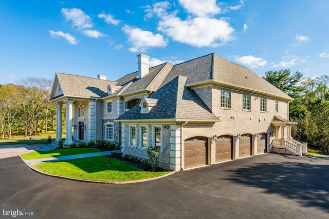 view of front of property with a front yard, driveway, a chimney, a garage, and brick siding