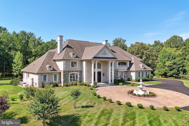 neoclassical / greek revival house featuring stone siding, a front yard, curved driveway, and a chimney