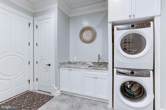 laundry area featuring light tile patterned floors, cabinet space, ornamental molding, a sink, and stacked washer and dryer