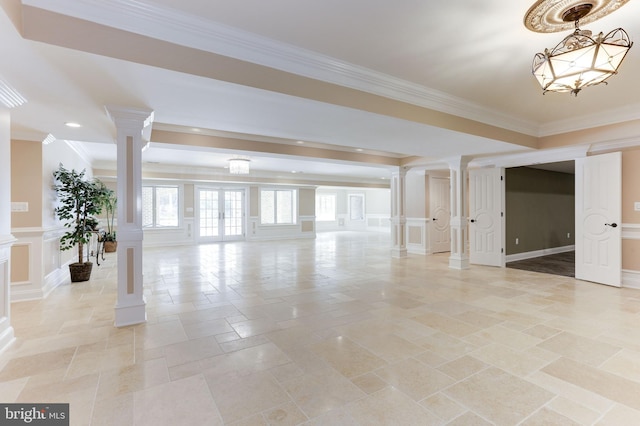 spare room featuring stone tile flooring, a decorative wall, crown molding, and ornate columns