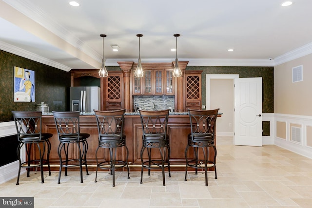 bar featuring visible vents, wet bar, ornamental molding, stainless steel refrigerator with ice dispenser, and wainscoting