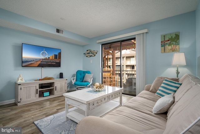 living room featuring visible vents, a textured ceiling, baseboards, and wood finished floors