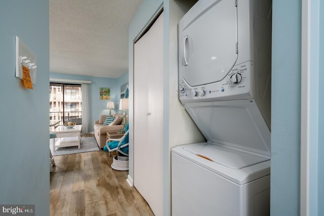 washroom with laundry area, a textured ceiling, stacked washing maching and dryer, and wood finished floors