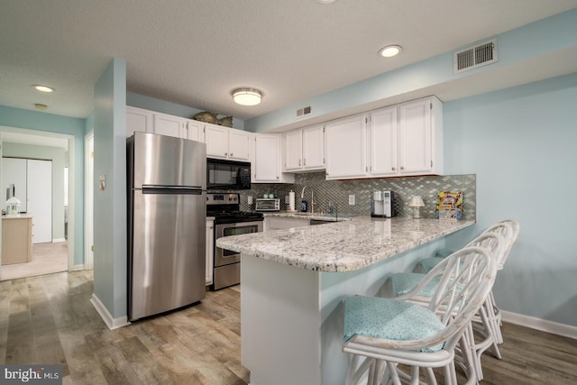 kitchen featuring visible vents, a peninsula, stainless steel appliances, white cabinets, and tasteful backsplash