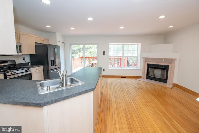 kitchen with dark countertops, light brown cabinetry, appliances with stainless steel finishes, light wood-style floors, and a sink