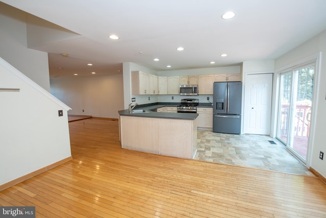 kitchen with a sink, dark countertops, light wood-style flooring, and stainless steel appliances