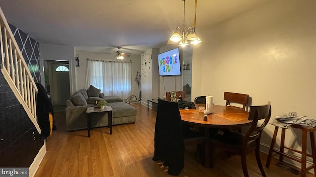 dining space with stairway, ceiling fan with notable chandelier, baseboards, and wood finished floors